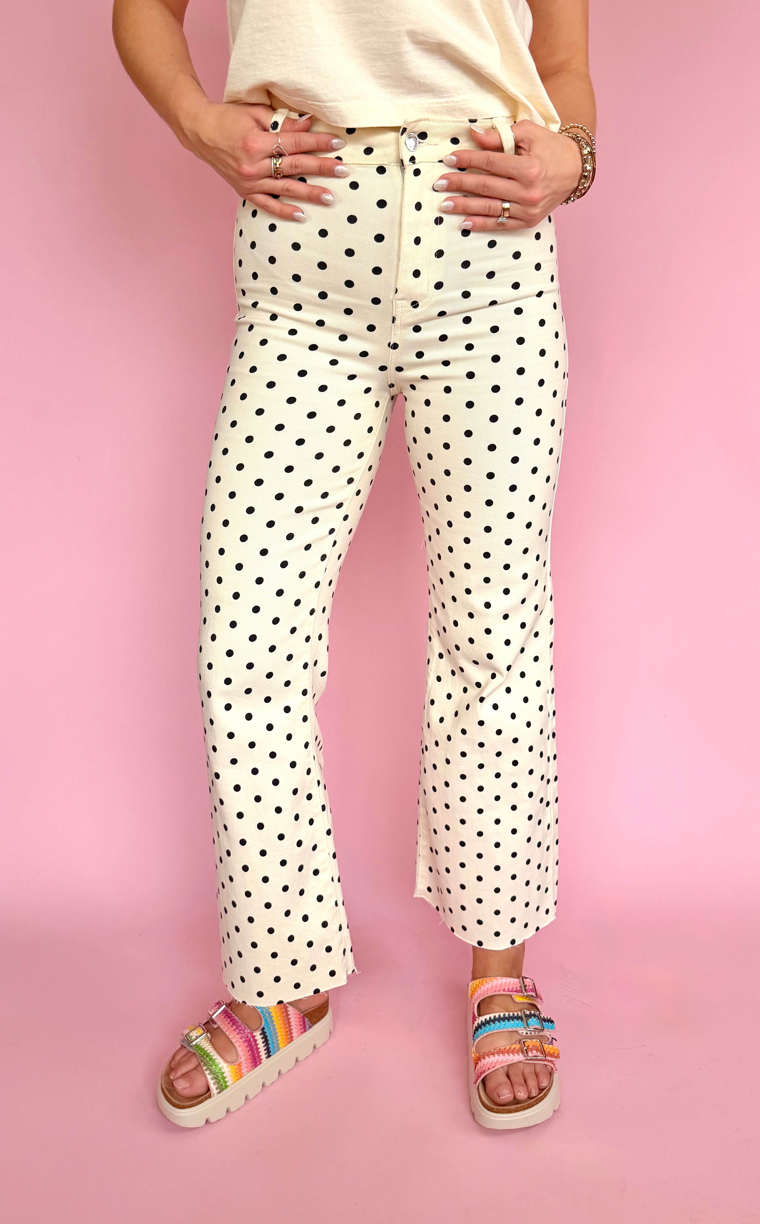 Person wearing polka dot pants and colorful sandals on a pink background, polka dot flare pant, raw hem bottom, high waisted jean, stretchy comfy summer pant