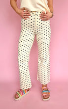 Person wearing polka dot pants and colorful sandals on a pink background, polka dot flare pant, raw hem bottom, high waisted jean, stretchy comfy summer pant
