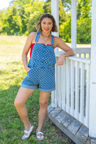 Woman in a blue polka dot dress standing on a grassy area with trees in the background, fun and playful, polkadot overall, summer comfort, effortless, USA, Americana 