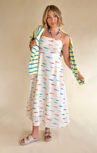 Woman wearing a colorful cardigan over a patterned dress on a beige background, maxi dress, spaghetti strap dress, rainbow, colorful, fish dress 