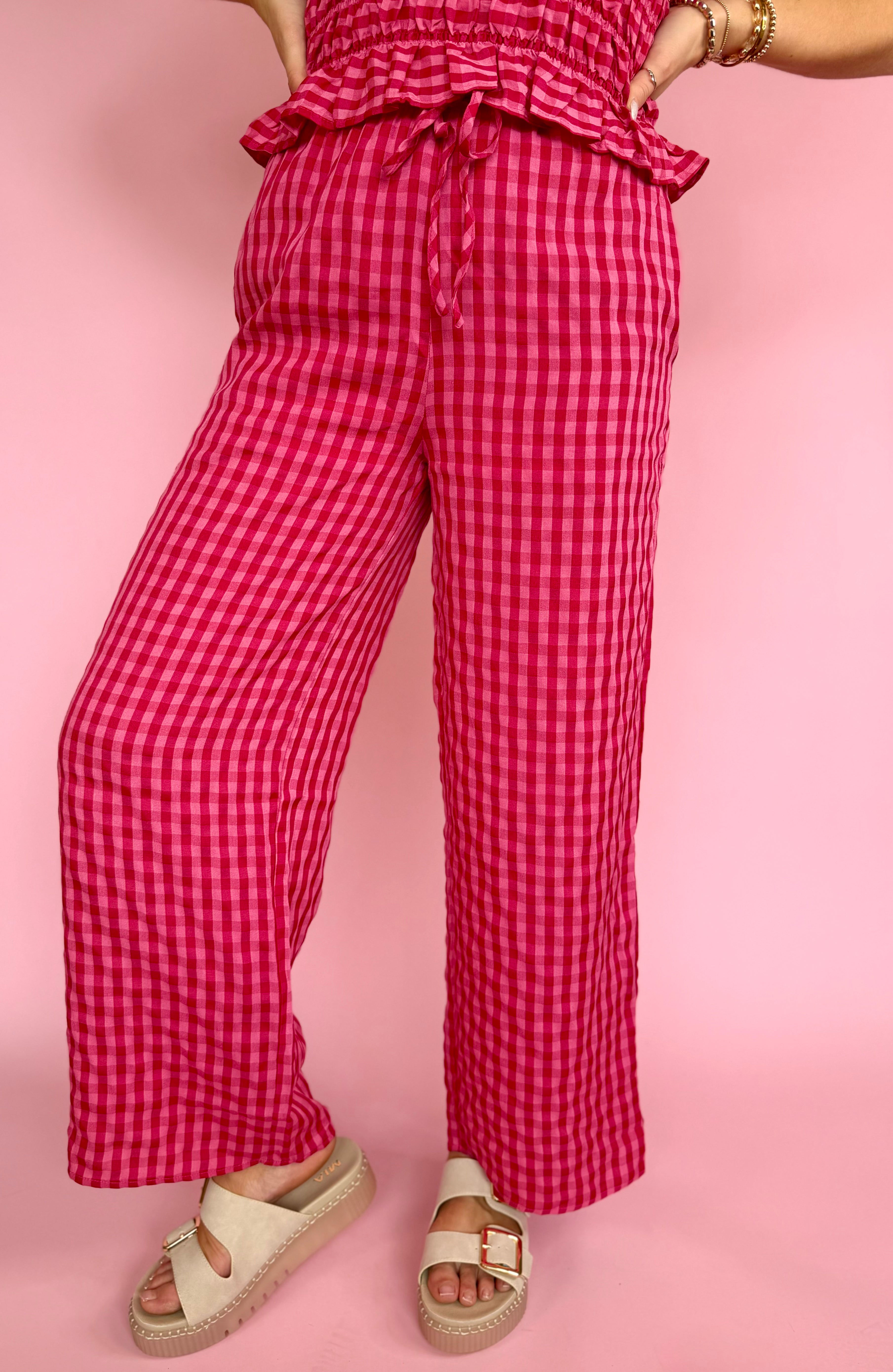 Person wearing red checkered pants on a pink background, draw string pant, wide leg lover, pink favorites, strawberry funk pant 