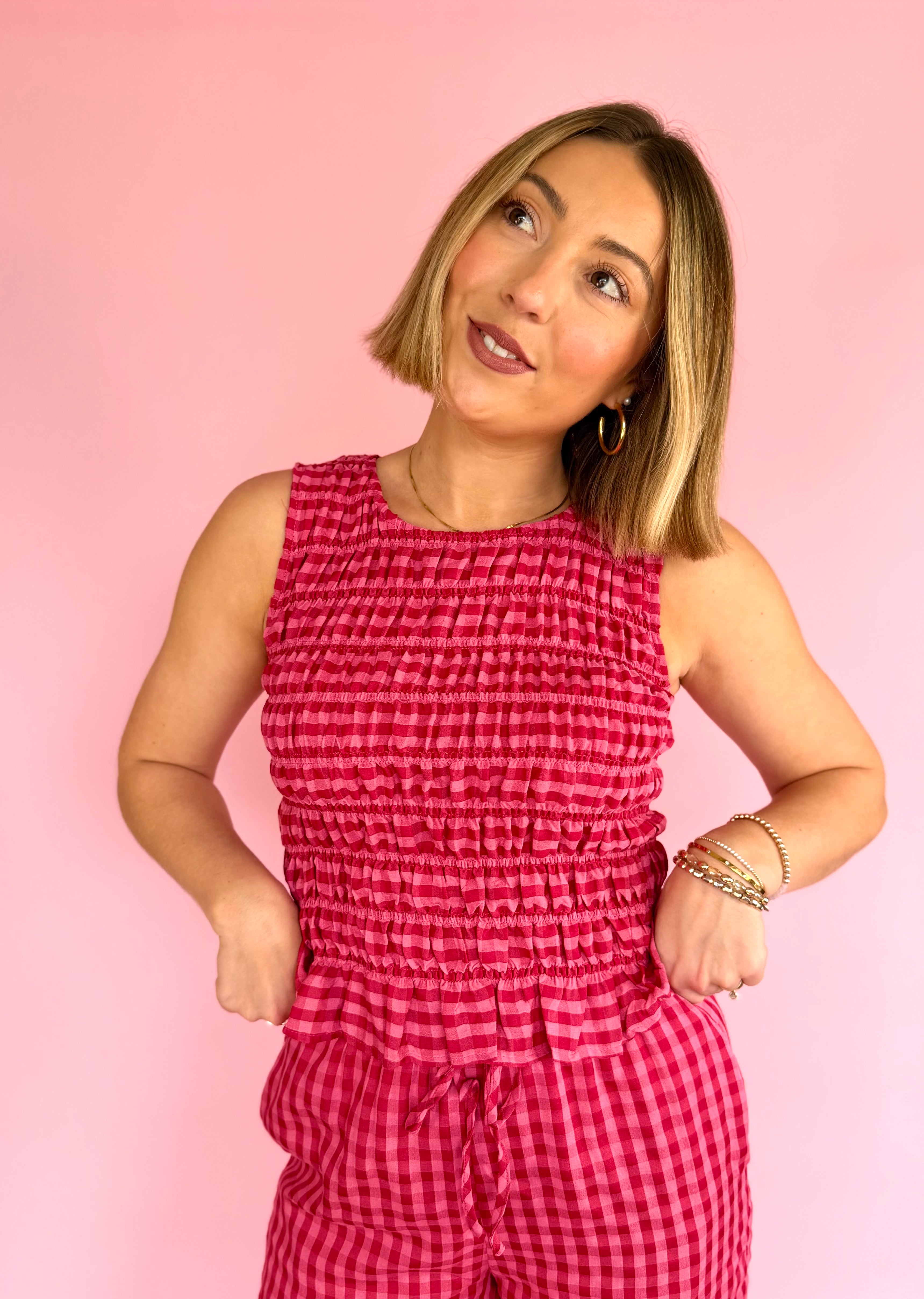 Woman wearing a pink checkered jumpsuit against a pink background, pink favorites, fitted smock tank, taste of strawberry, flared hem tank, full length summer tank 