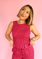 Woman wearing a pink checkered jumpsuit against a pink background, pink favorites, fitted smock tank, taste of strawberry, flared hem tank, full length summer tank 