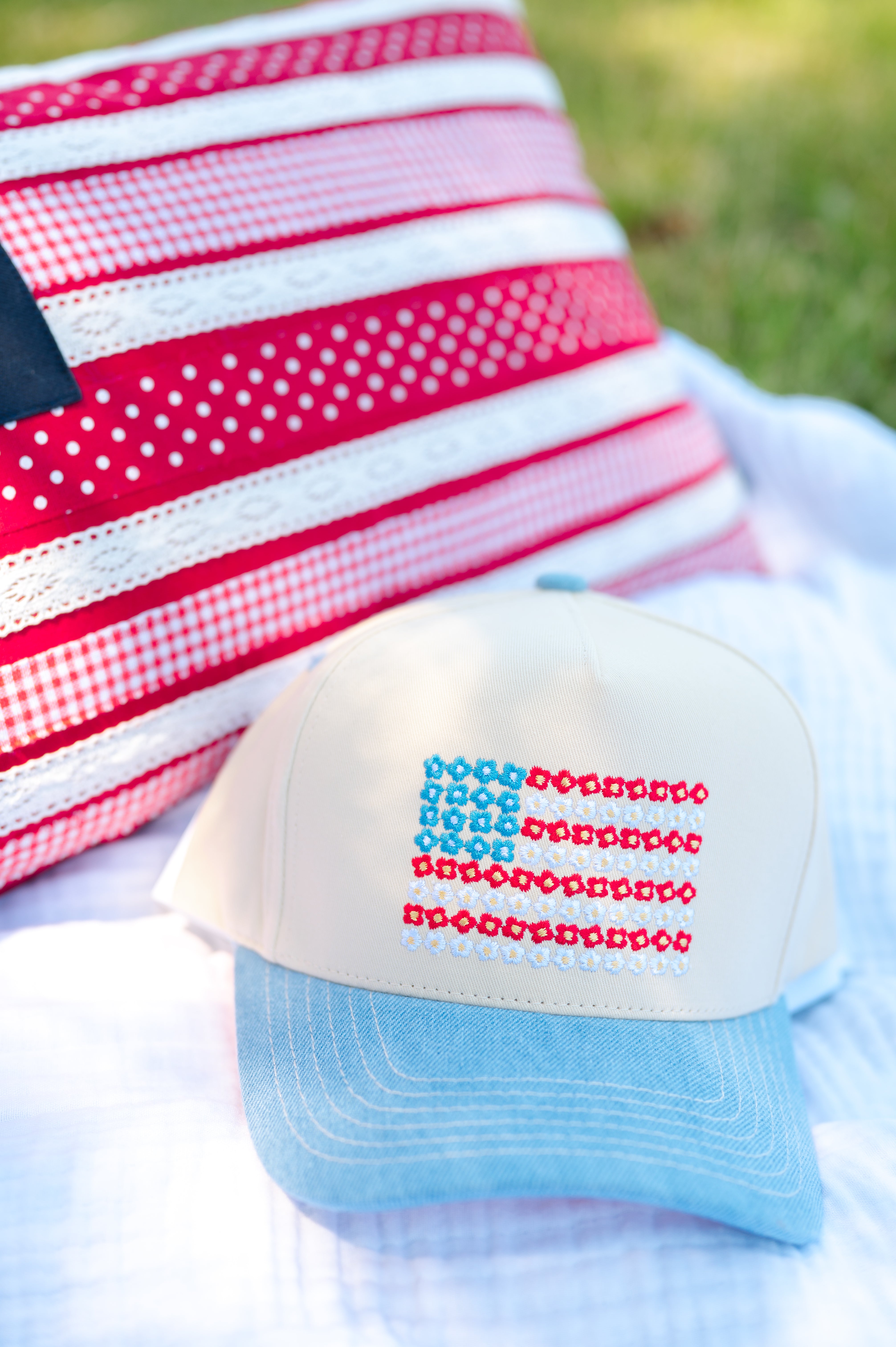 Cap with American flag design on a white blanket with a red and white checkered fabric in the background, red white and blue, flower power, stars and stripes, denim hat
