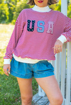 Person wearing a red and white striped shirt with 'USA' print, denim shorts, and white sneakers outdoors, USA, americana, striped, patchwork