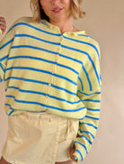 Person wearing a yellow and blue striped sweater against a beige background, yellow and blue sweater, button up sweater, stripe sweater, summer sweater