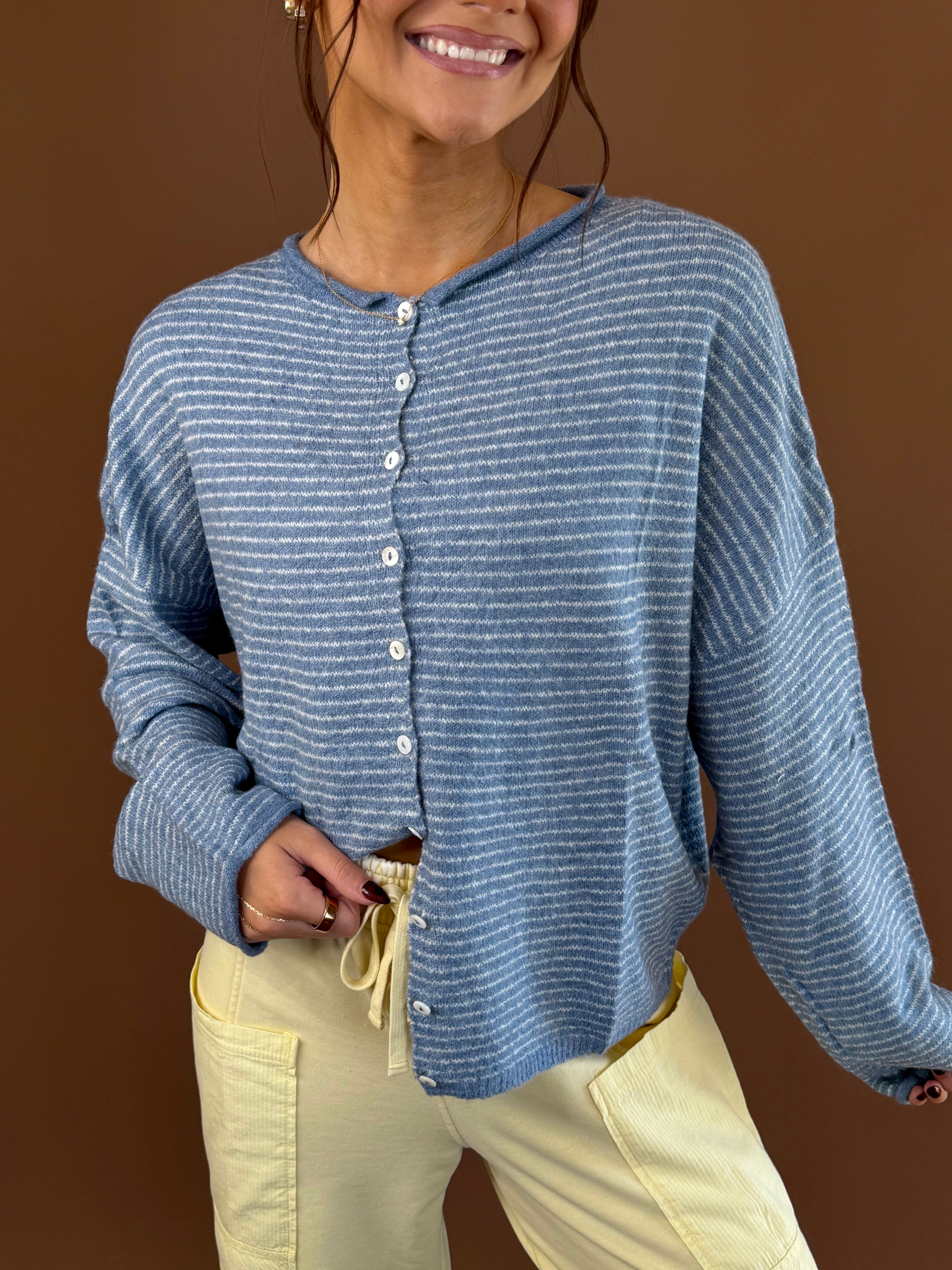 Model wearing a dusty blue pinstripe button-front cardigan with long sleeves, styled with pale yellow pants.