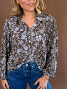 Bluebell Banter women's blouse with blue florals on an olive-brown background, crinkled texture, a collar, and long lantern sleeves.