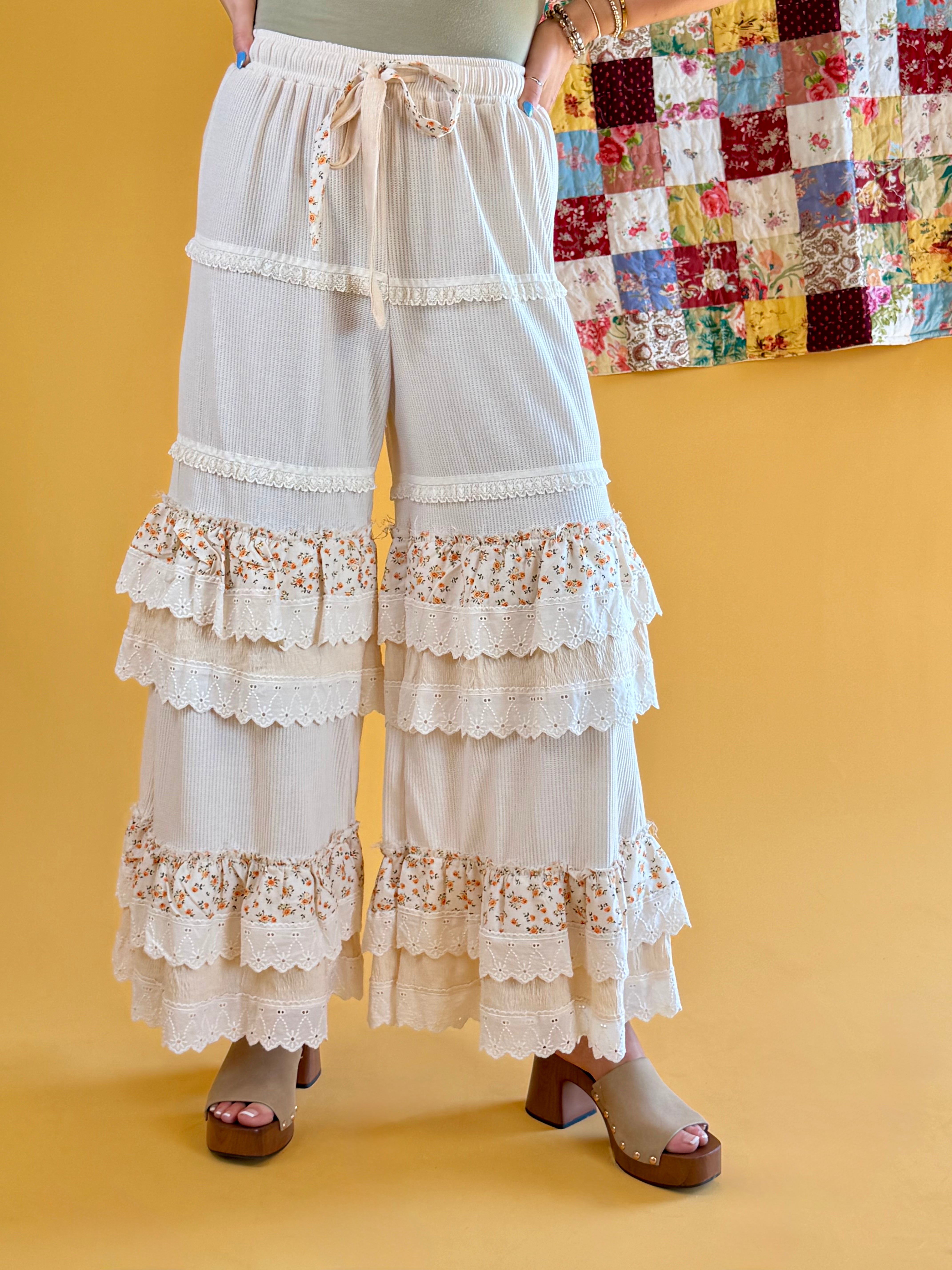 White tiered lace pants with floral trim worn by a person on a yellow background, boho pants, beachy, floral wide leg, ruffles, lace, tall girl friendly