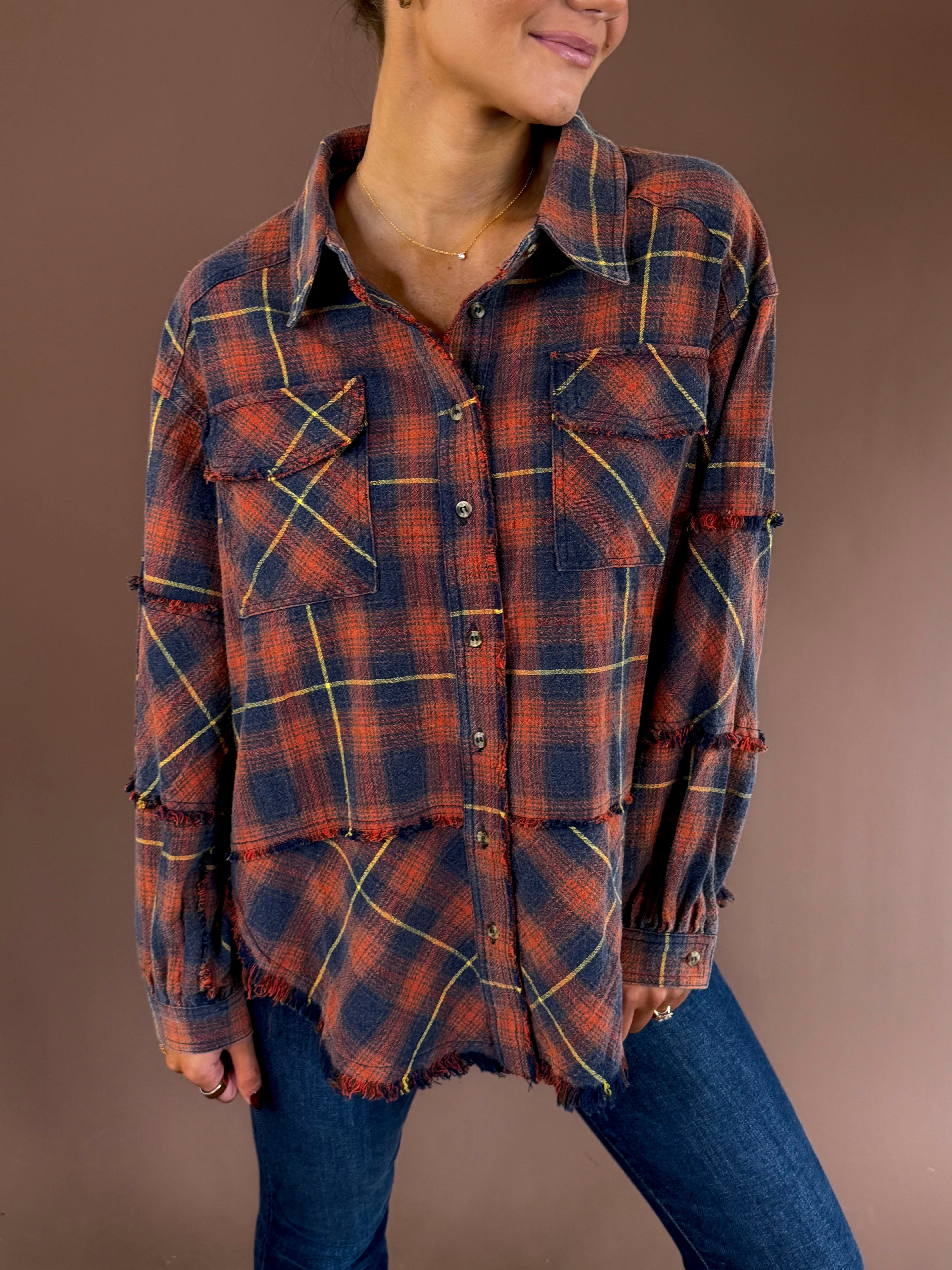 Model wearing the Bonfire Nights navy and orange plaid mineral-wash flannel with a button front, chest pockets, and raw hem, paired with jeans.