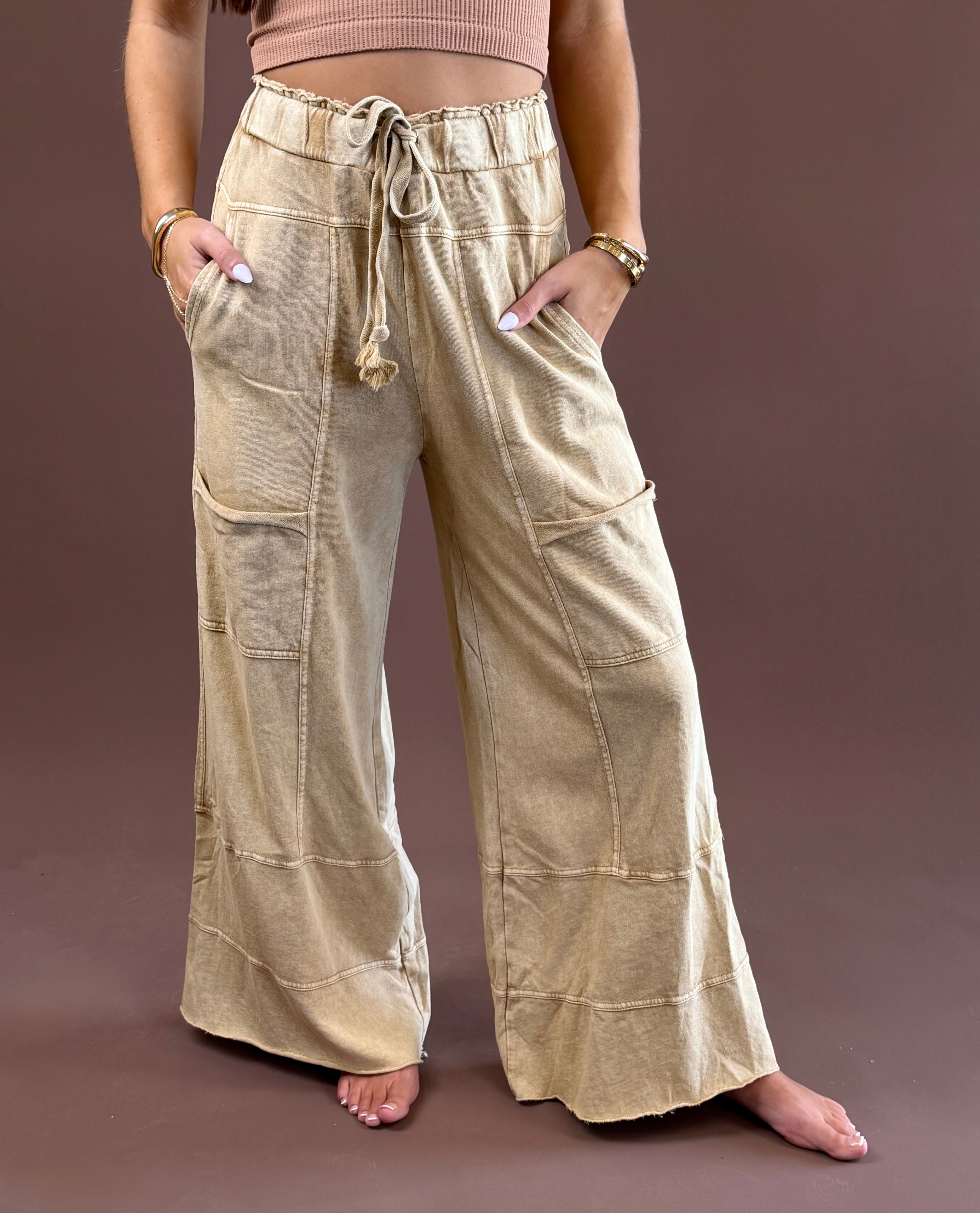 Camel Mist women’s mineral-wash pants with a relaxed wide-leg silhouette, elastic drawstring waist, roomy pockets, and raw-edge hems