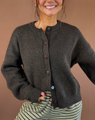 Model wearing a chocolate brown button-front cardigan with long sleeves and a round neckline, styled with striped pants.