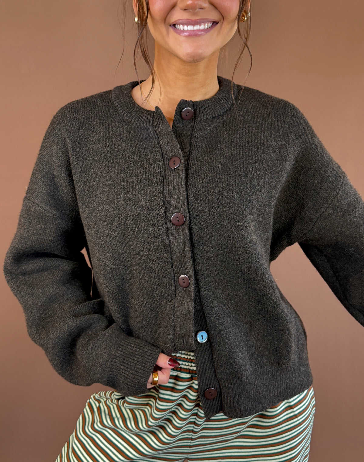 Model wearing a chocolate brown button-front cardigan with long sleeves and a round neckline, styled with striped pants.