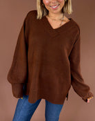 Model wearing the Forever Favorite chestnut brown oversized V-neck sweater with long sleeves and ribbed cuffs, paired with blue jeans.