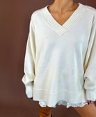 Model wearing the Forever Favorite cream oversized V-neck knit sweater with long sleeves and wide ribbed trim over white lace-trim shorts.