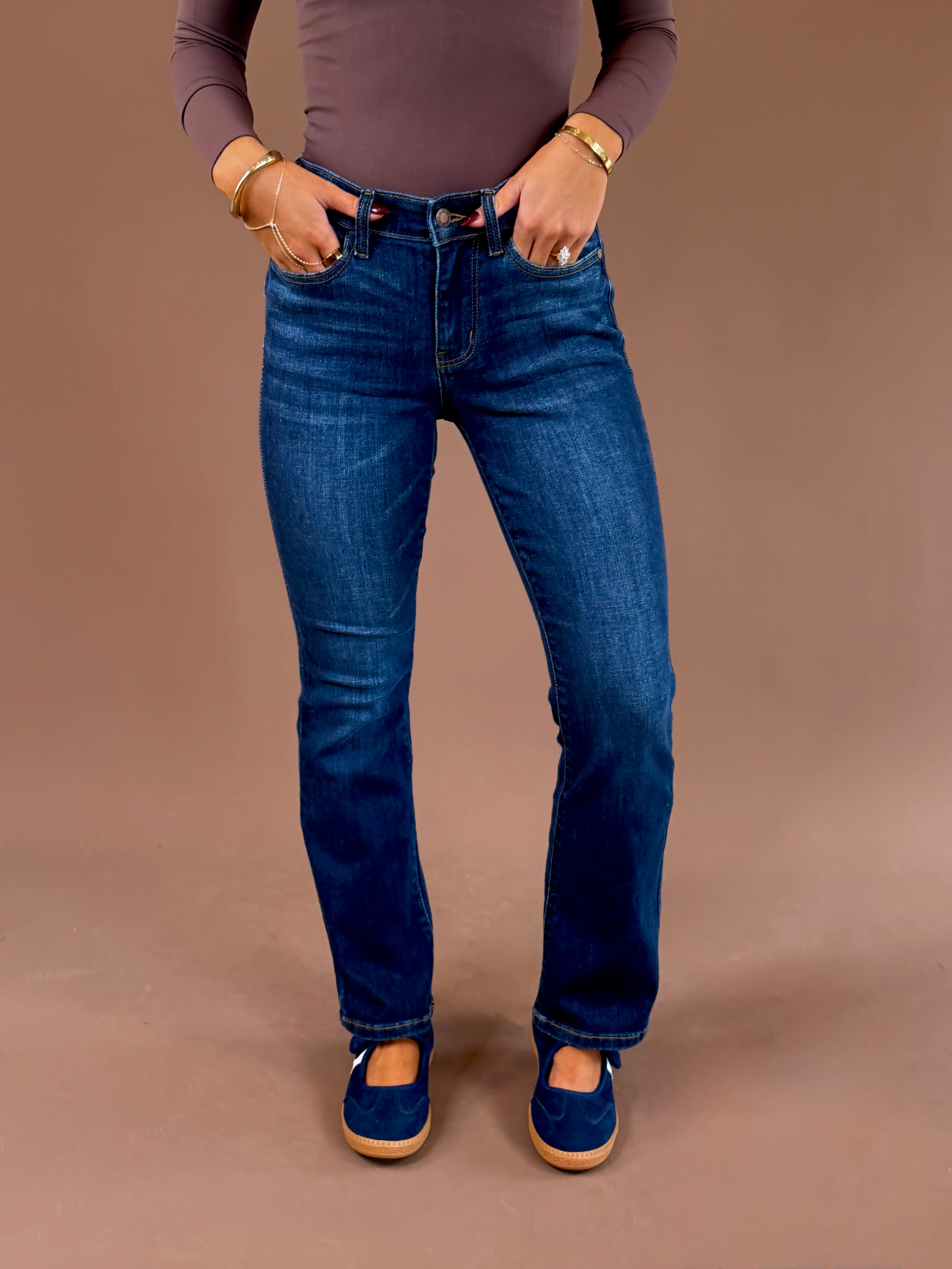 Front view of a model wearing Judy Blue dark wash mid-rise bootcut jeans with a 29-inch inseam, styled with a brown top and blue shoes.