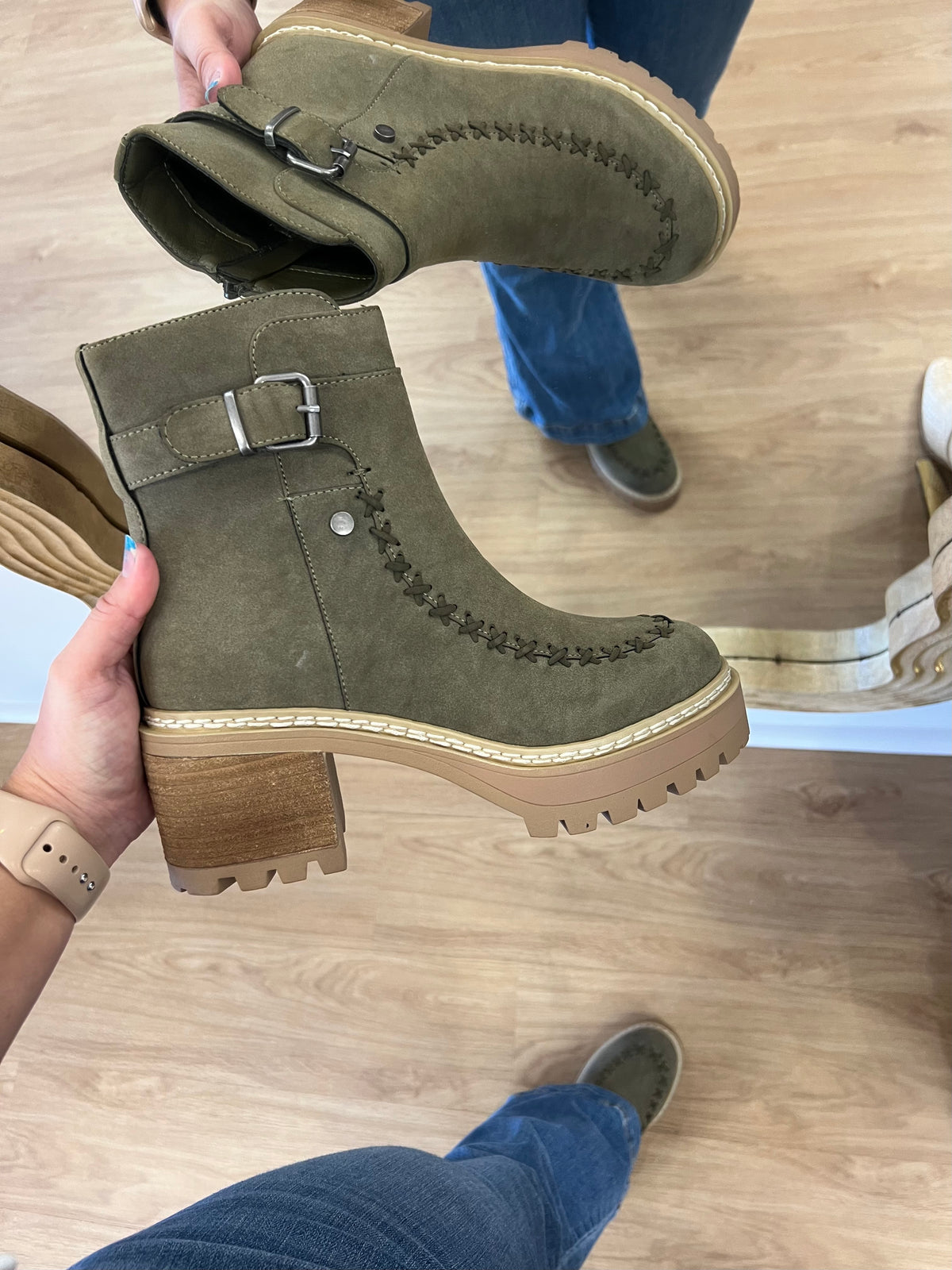 Olive green faux-suede ankle boots with a side buckle accent, decorative stitched seams, a zipper closure, and a chunky stacked heel on a platform lug sole.