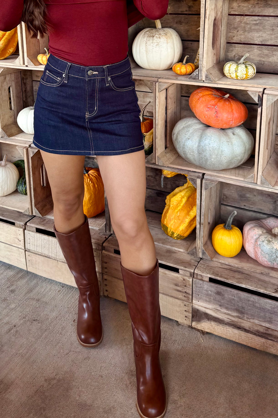 Dark wash high-rise denim mini skirt with classic five-pocket styling and contrast stitching, worn with brown knee-high boots.