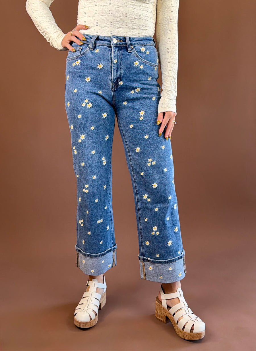 MICA Take it Back women's medium-wash high-rise wide-leg jeans with floral daisy embroidery and adjustable turned-up cuffs.
