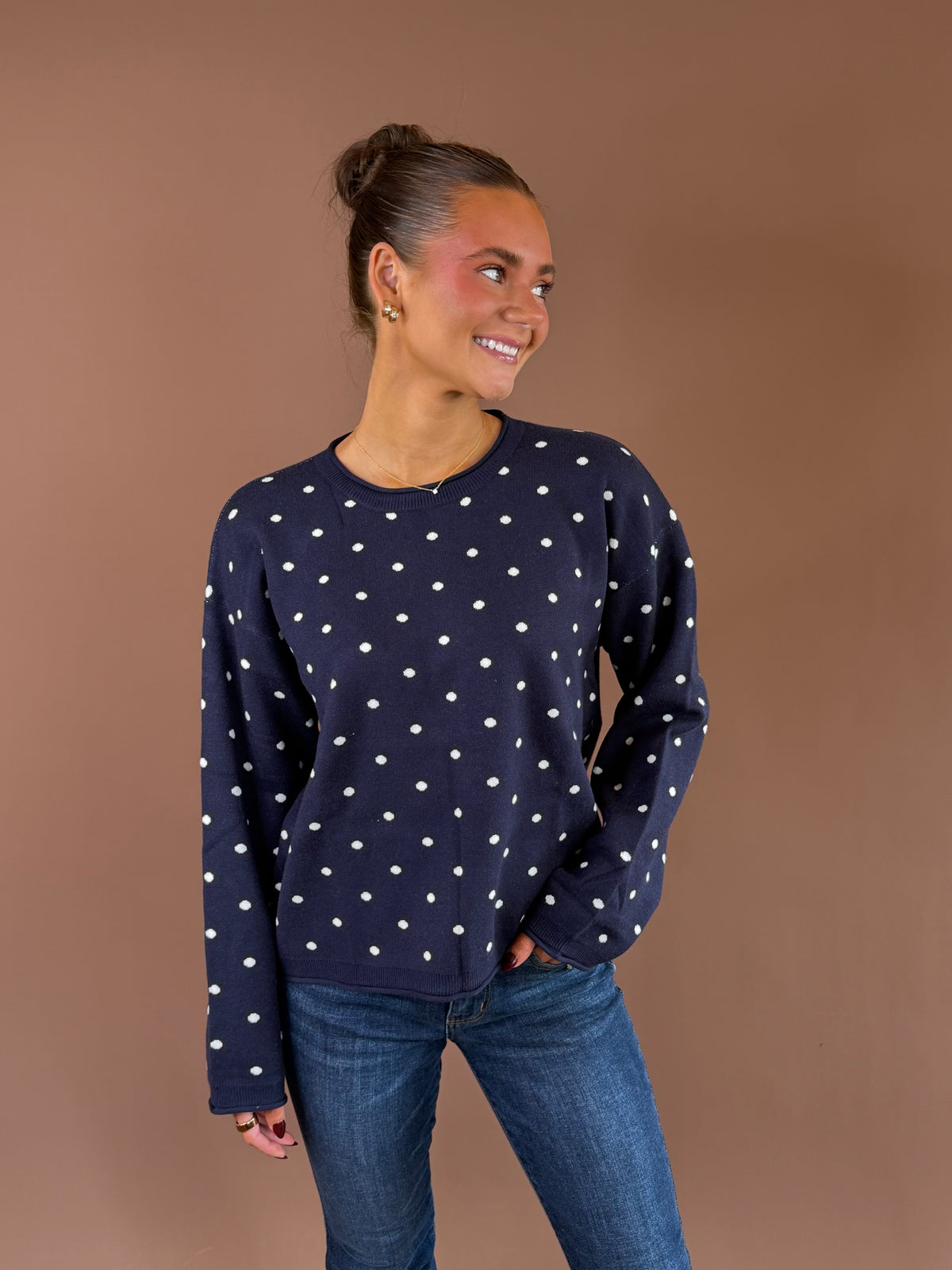 Model wearing the On the Dot navy crewneck sweater with ivory polka dots and long sleeves, paired with blue jeans.