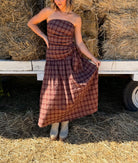 Model wearing a burgundy multicolor plaid strapless wrap dress with an adjustable side tie and a flowy full-length skirt.