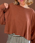 Model wearing a chestnut relaxed long sleeve cotton top with a round neckline, styled with green striped pants.