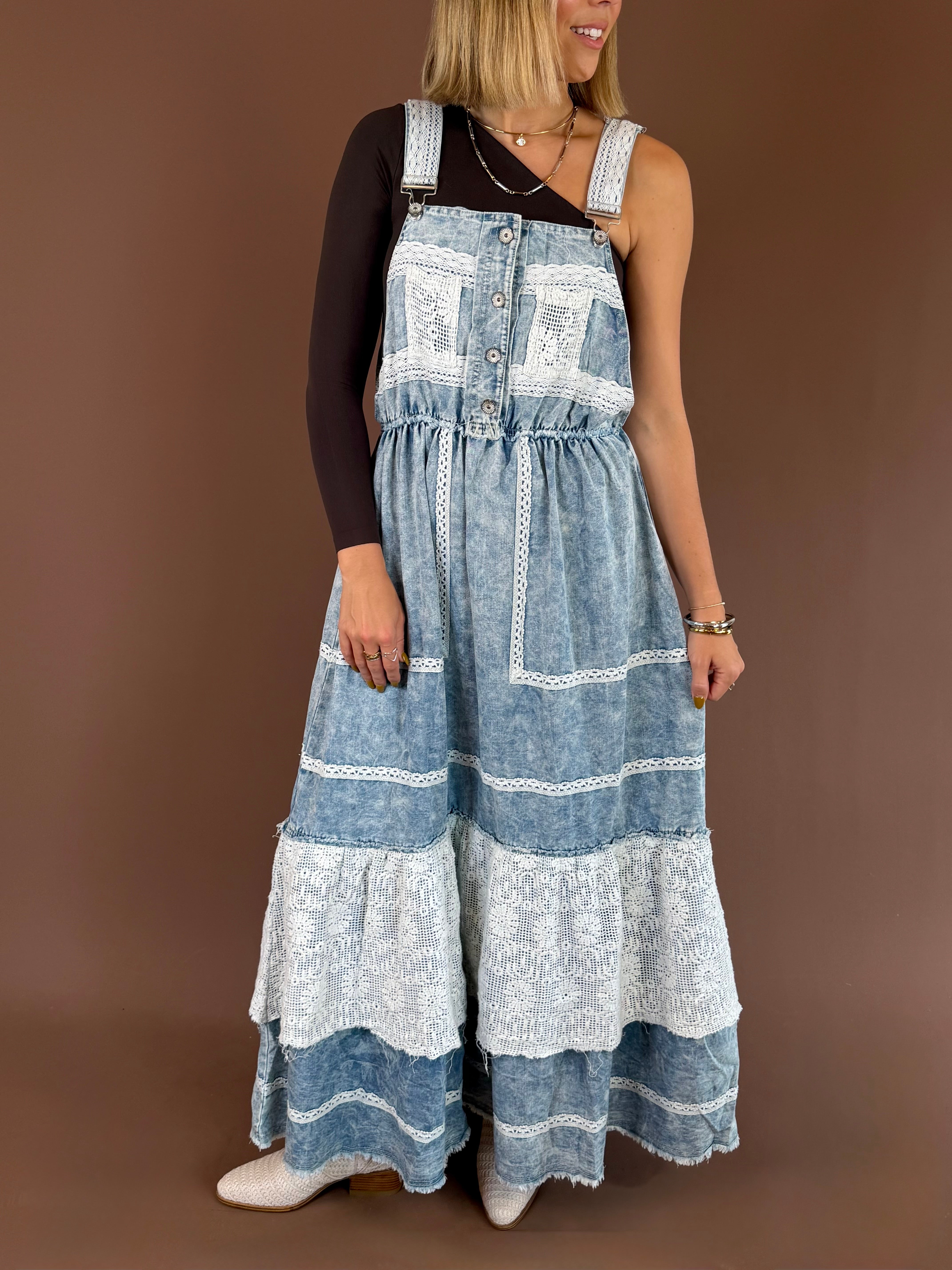 Model wearing the POL Blue Jean Daydream maxi overall dress with mixed-wash denim panels, crochet lace details, and patch pockets over a black top.