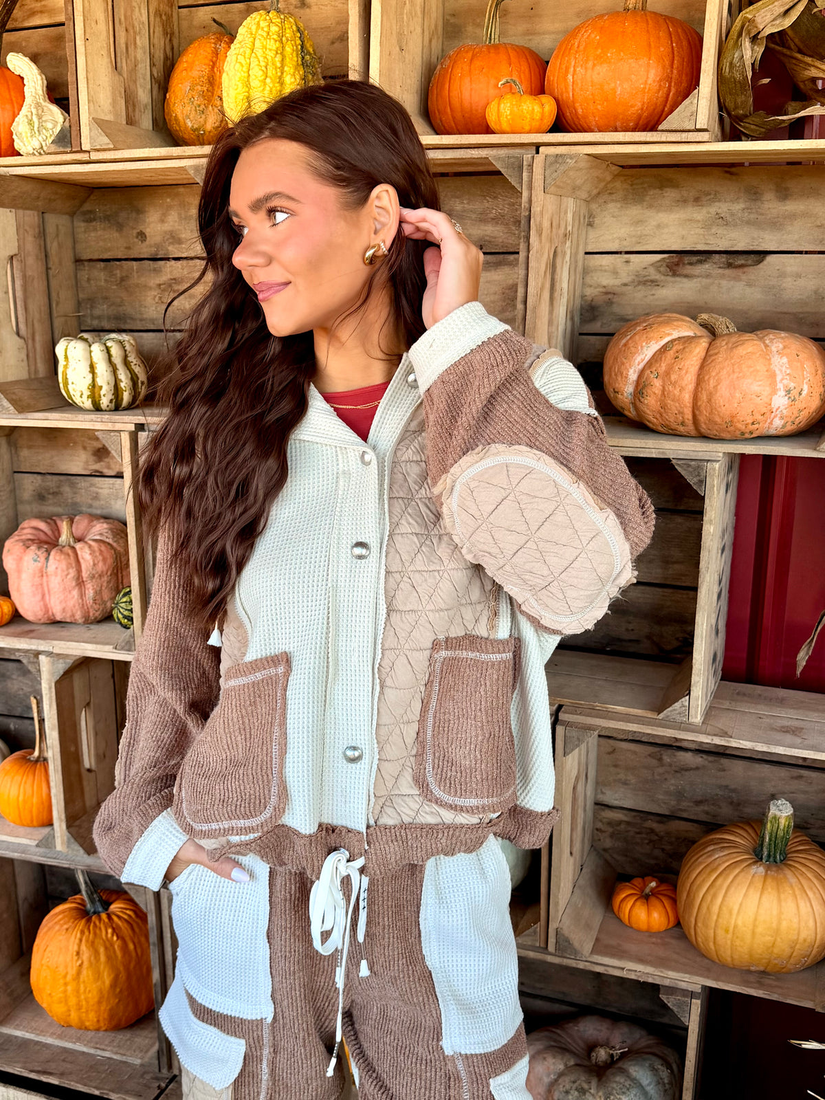 Model wearing an oat and chocolate brown patchwork hooded jacket mixing quilted and thermal textures with a button-front closure and front pockets.