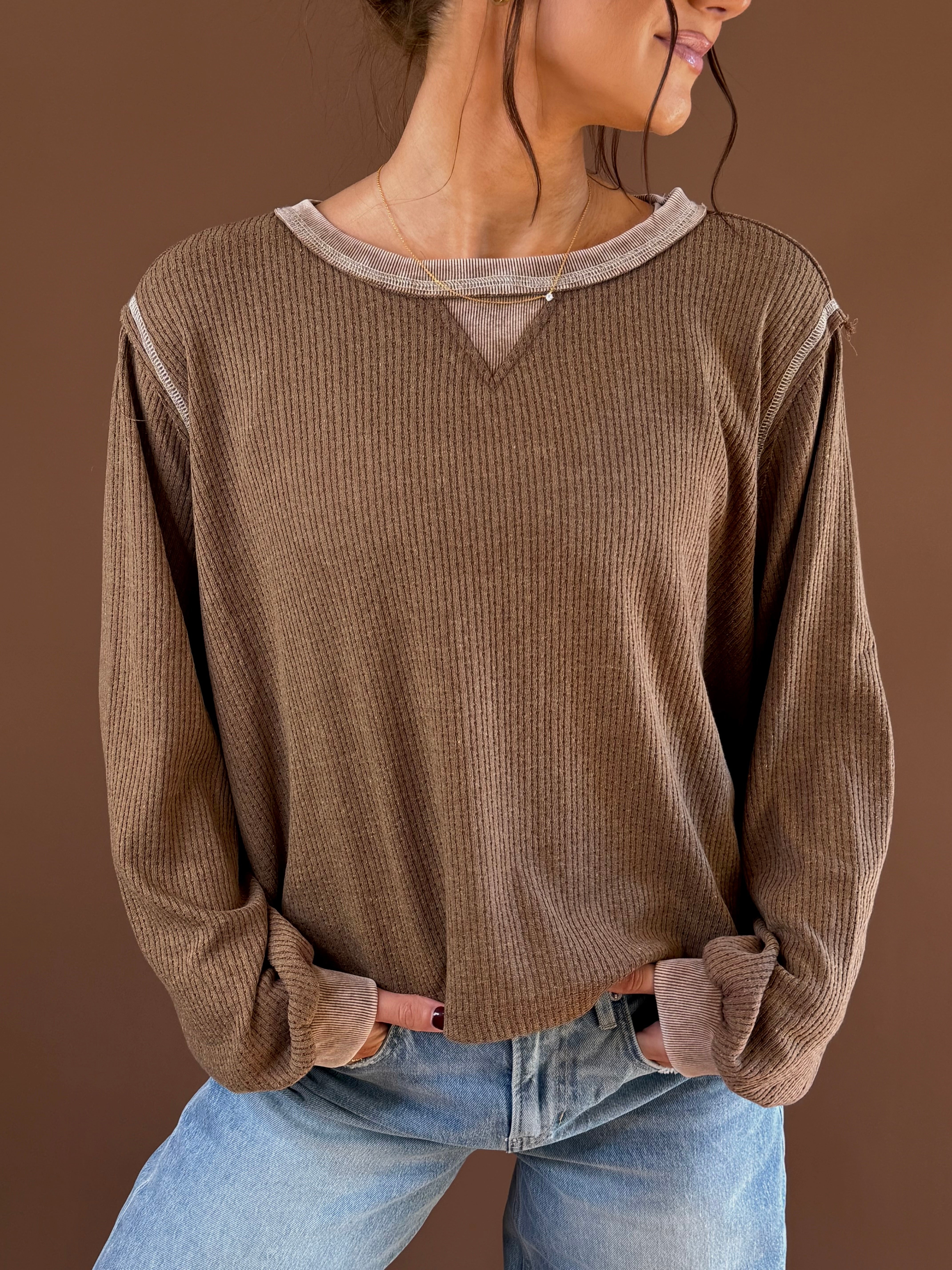 Model wearing a chocolate vintage wash long sleeve knit top with ribbed texture and contrasting neckline trim, styled with jeans.