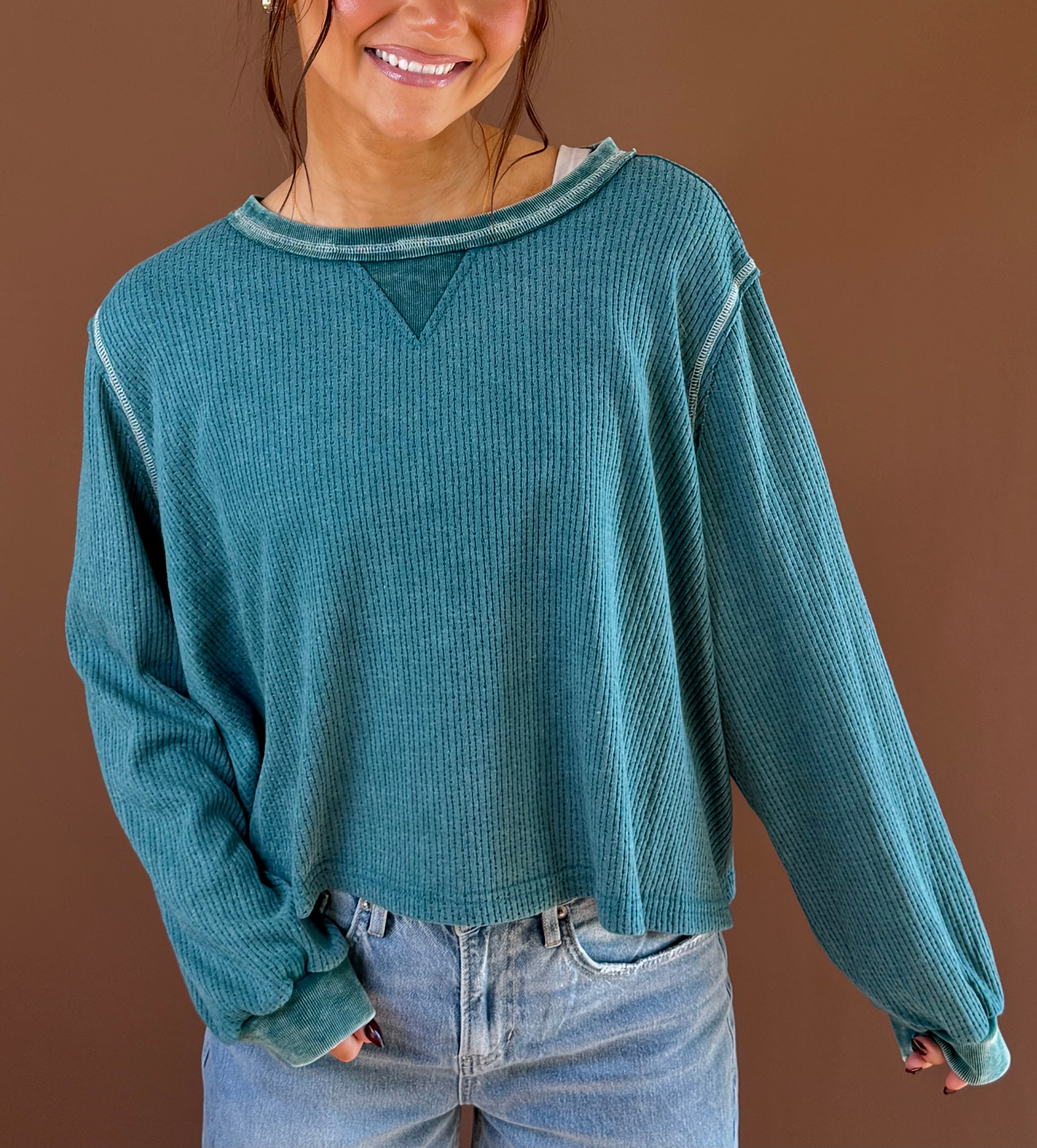 Model wearing an evergreen vintage wash long sleeve knit top with ribbed texture and seam details, styled with jeans.