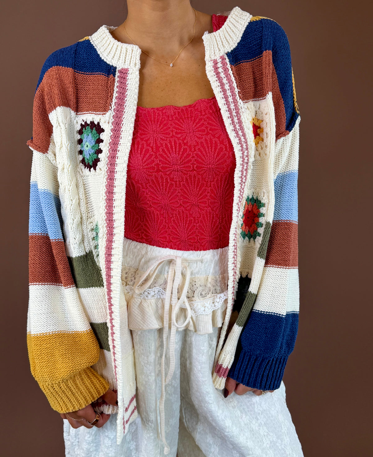 Model wearing the POL Road Trip striped open-front cardigan with multicolor granny-square pockets over a red top and light drawstring pants.
