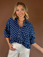 Navy blue polka dot button-down blouse with three-quarter sleeves, relaxed fit, and a ruffled hem.