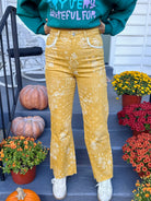 Model wearing mustard yellow bandana paisley print flare jeans with front pockets and frayed hems, styled with a green graphic sweatshirt and white sneakers.