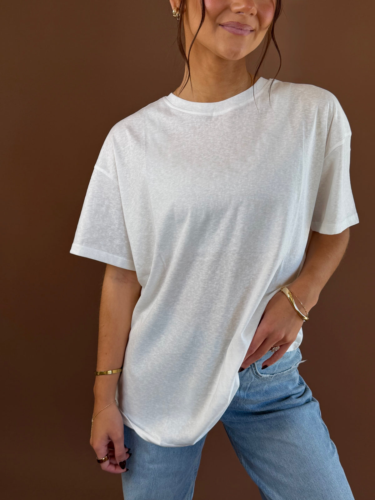Model wearing a white relaxed boyfriend T-shirt with a round neckline and short sleeves, styled with blue jeans.