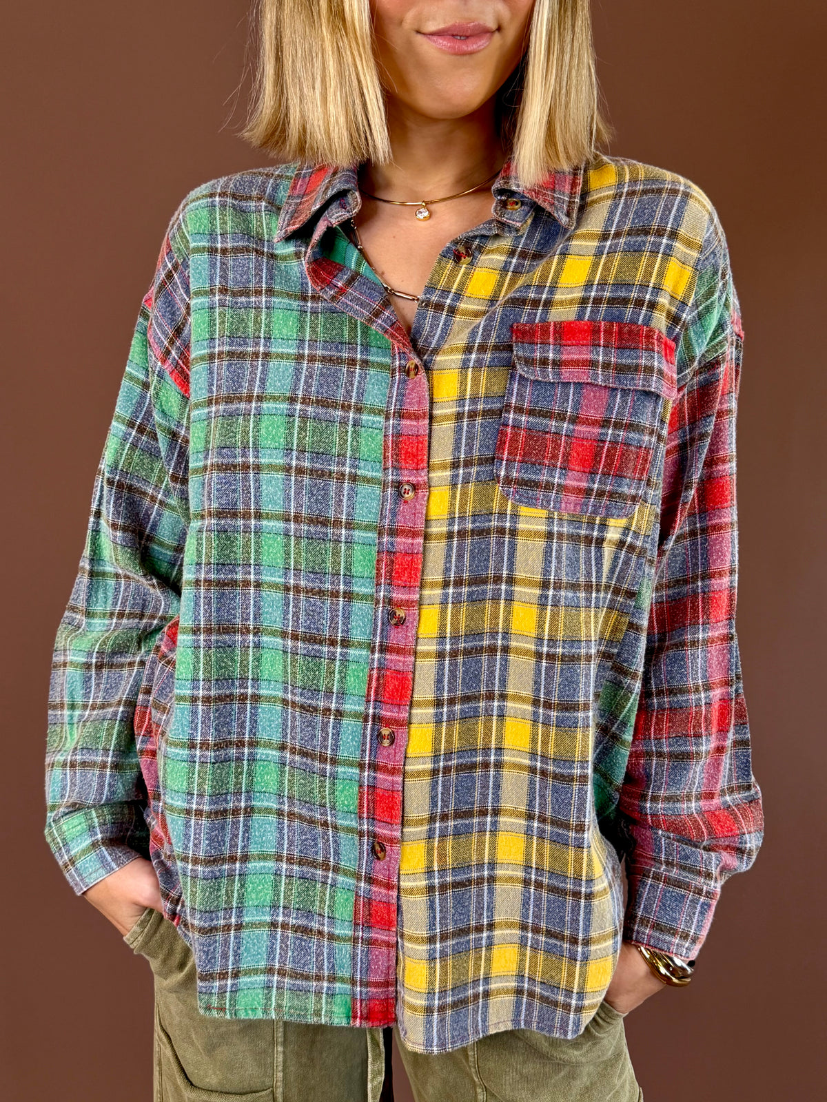 Model wearing the ROYally Cute oversized button-front flannel with green, blue, yellow, and red mixed plaid panels, paired with olive pants.
