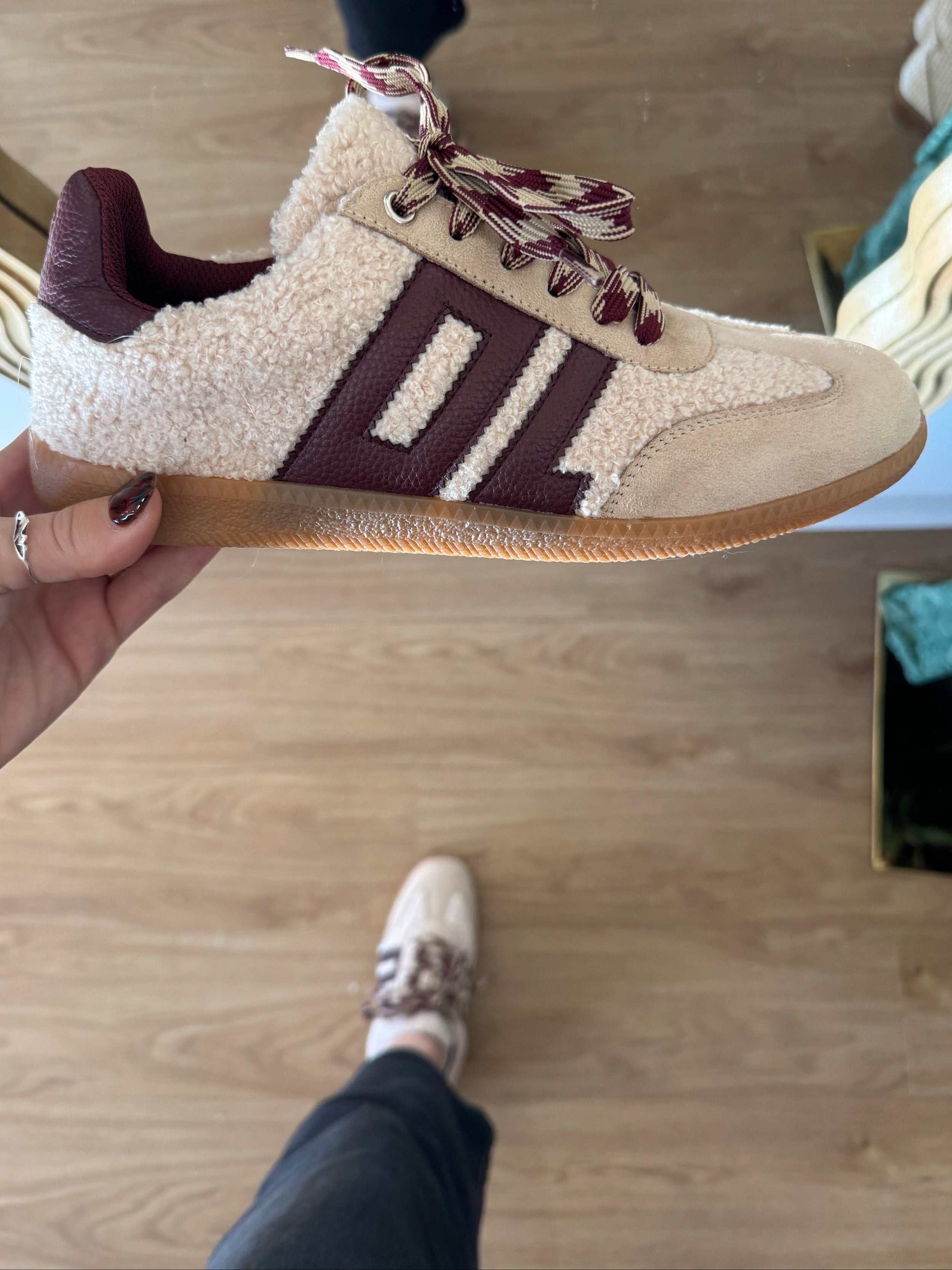 Beige and brown sneaker with decorative elements held by a hand on a wooden floor.