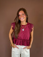 Wine-colored cotton top with a round neckline, cap sleeves, side lace trim, exposed seams, and ruffled hem.