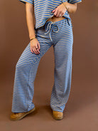 Model wearing dusty blue, yellow, and tan striped wide leg lounge pants with a drawstring waist and matching striped tee.