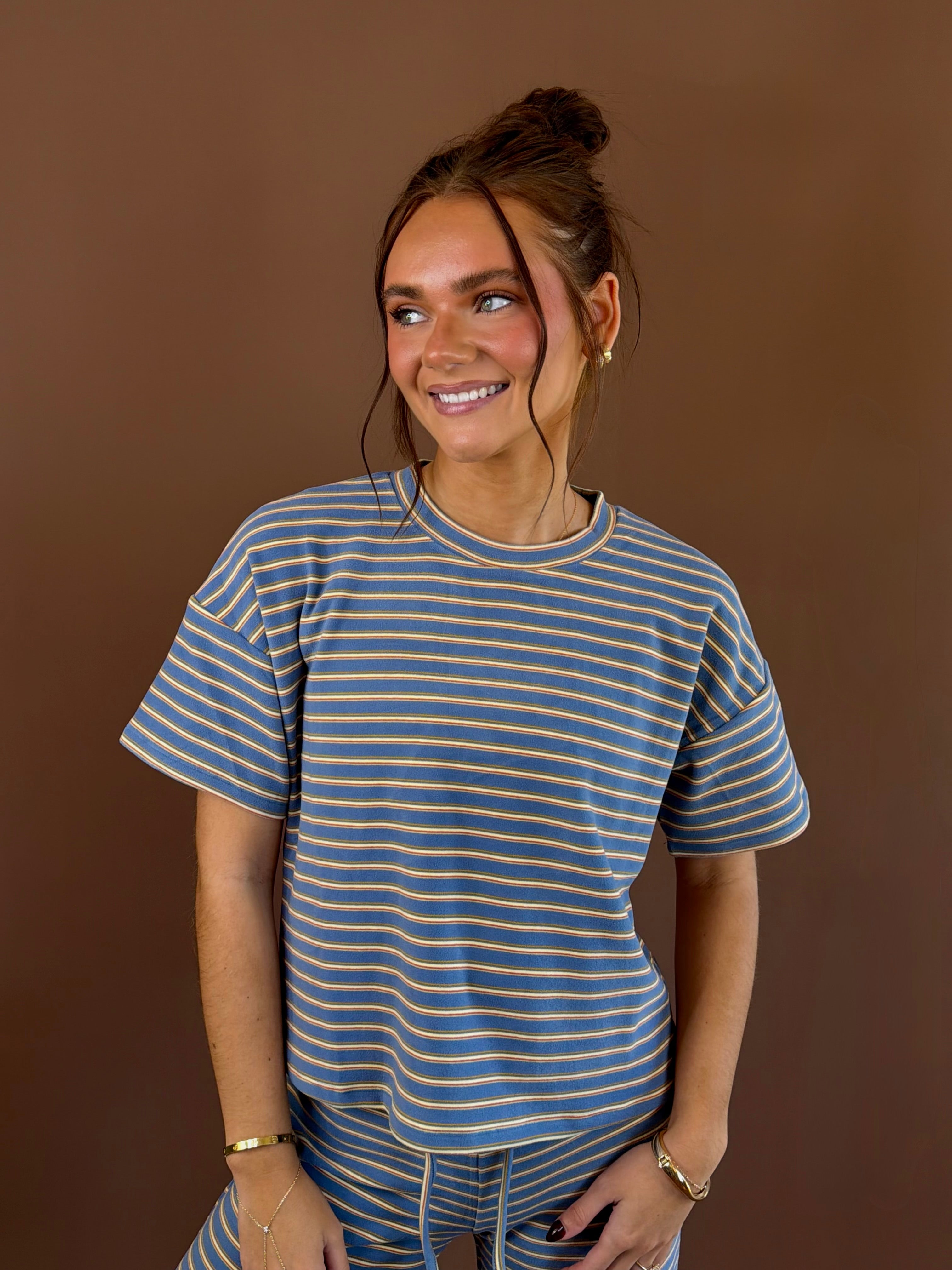 Model wearing a dusty blue short sleeve tee with yellow and tan stripes, a round neckline, and a relaxed silhouette.